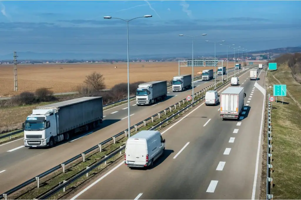 Highway transportation with a convoy of white Lorry trucks passing trucks and vans
