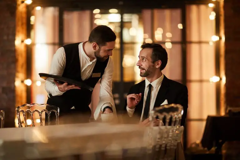 mature bearded businessman talking to waiter bringing coffee and smiling happily in luxury restaurant