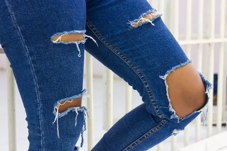 legs of woman standing wearing torn jeans worn