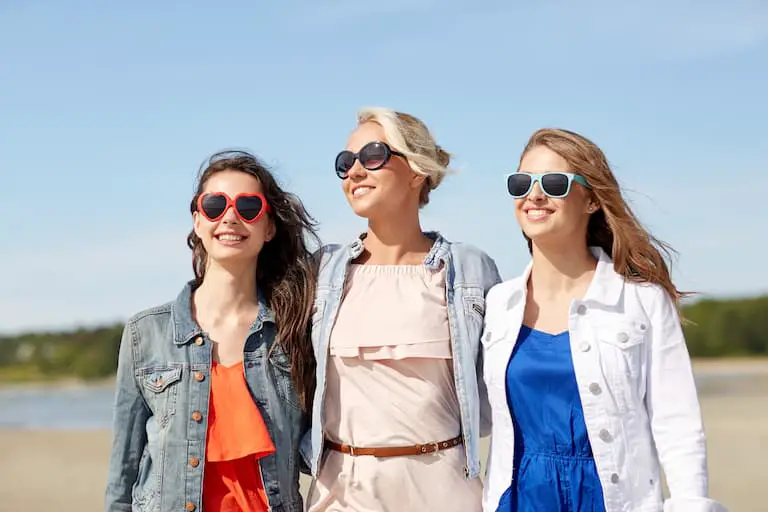 group of smiling young women in sunglasses and casual clothes